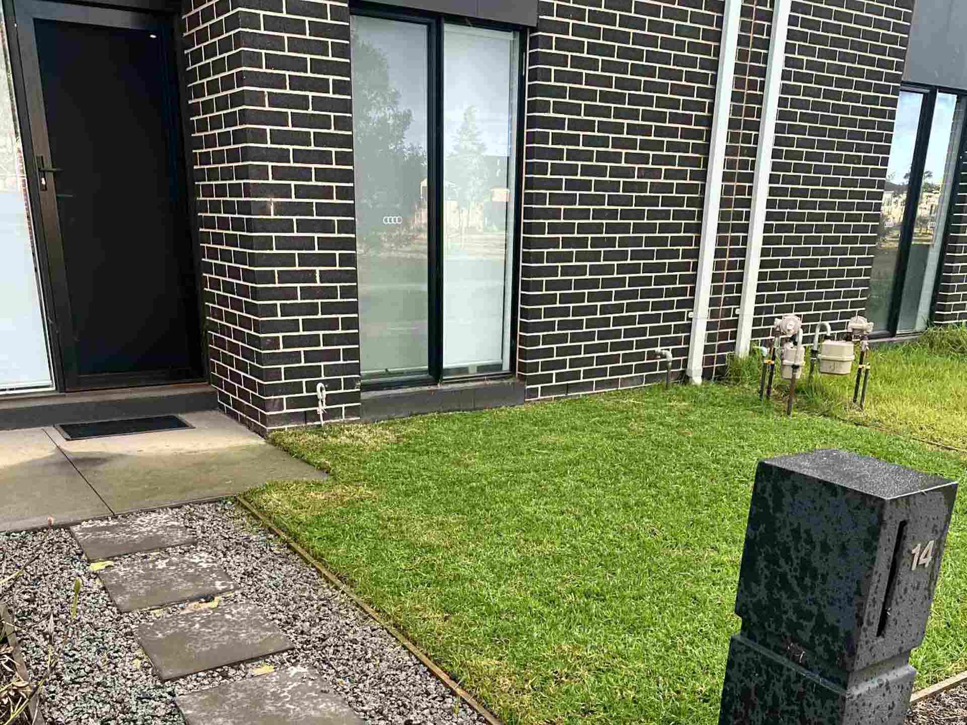 1-home-ndis-comp Neat front lawn and stepping-stone gravel path at a dark brick townhouse