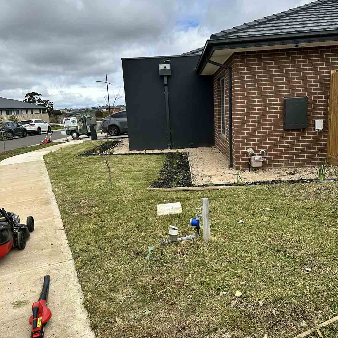 After: mown lawn and edged garden bed beside the brick house, with a mower on the path