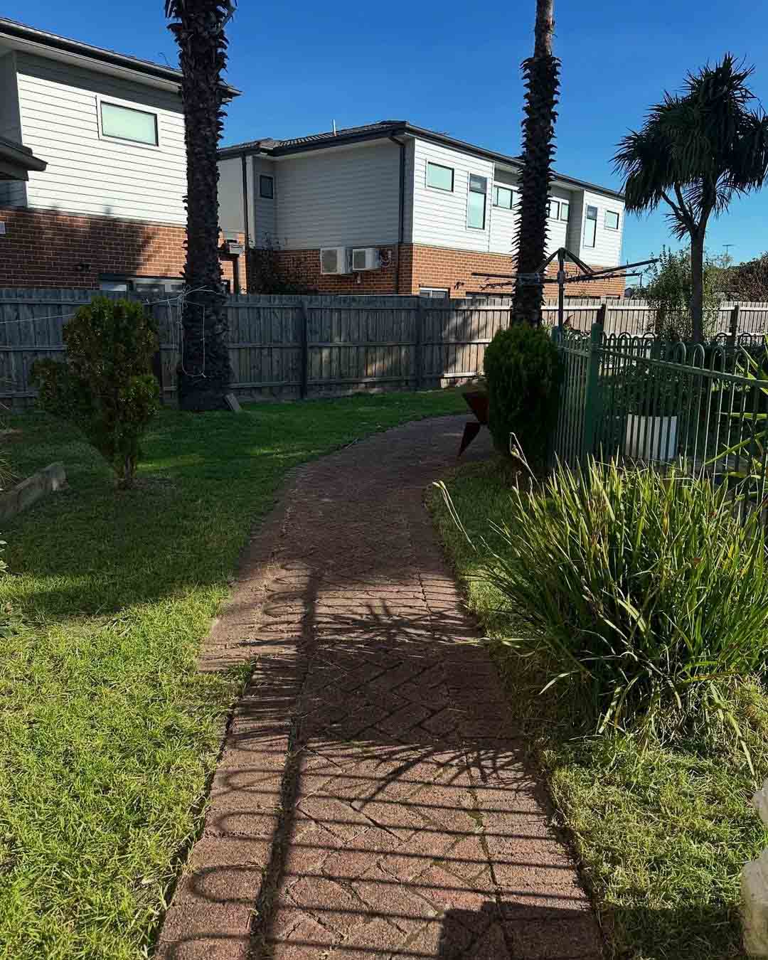 Brick-paved garden path through a tidy lawn with palm trees