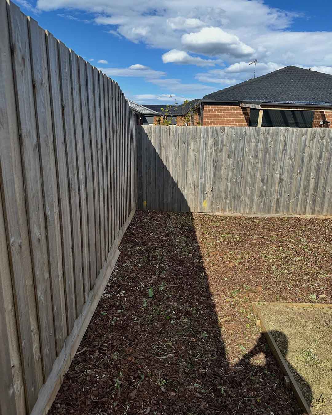 Cleared garden bed of dark soil along a timber paling fence