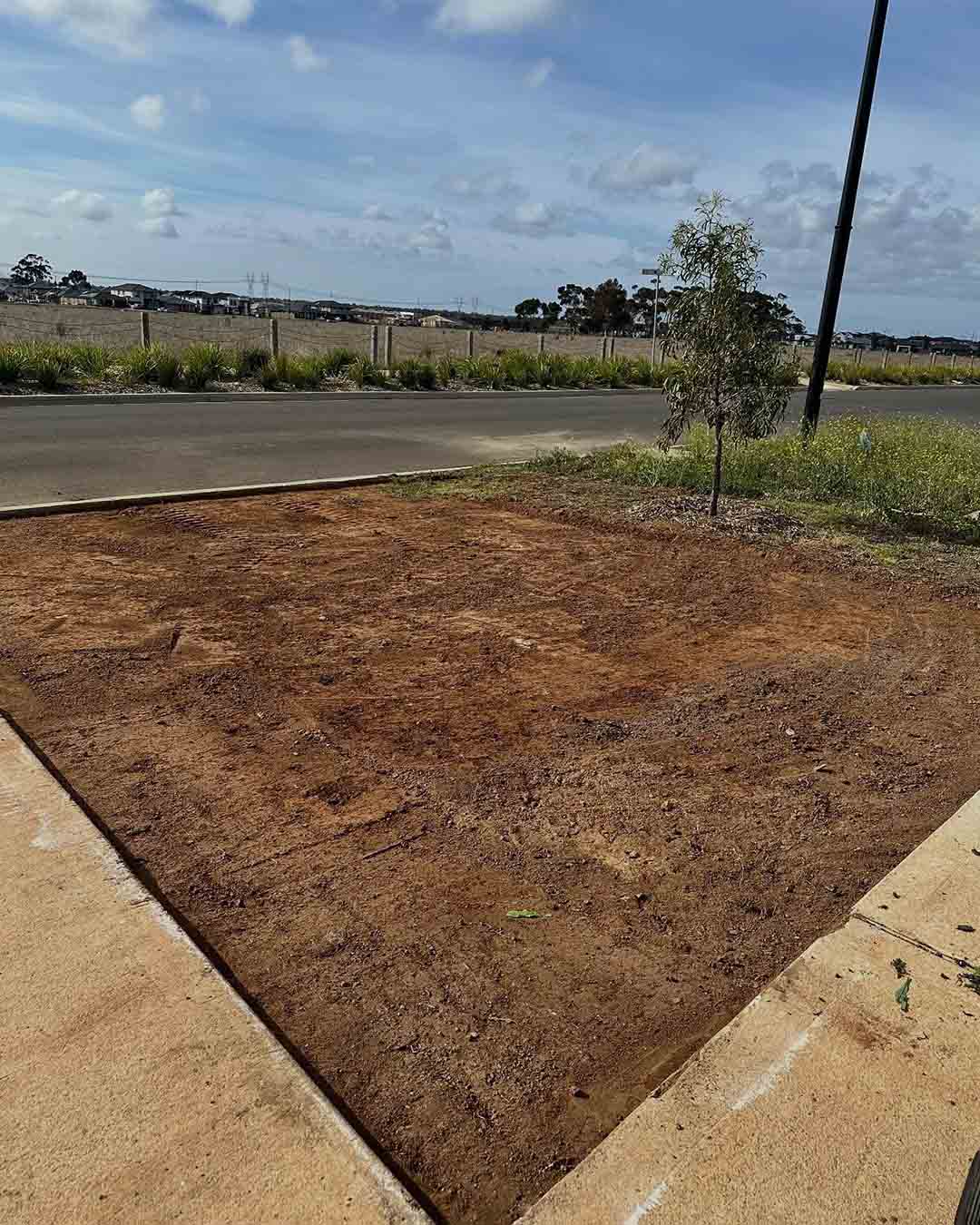 Levelled area of bare soil beside a footpath and road