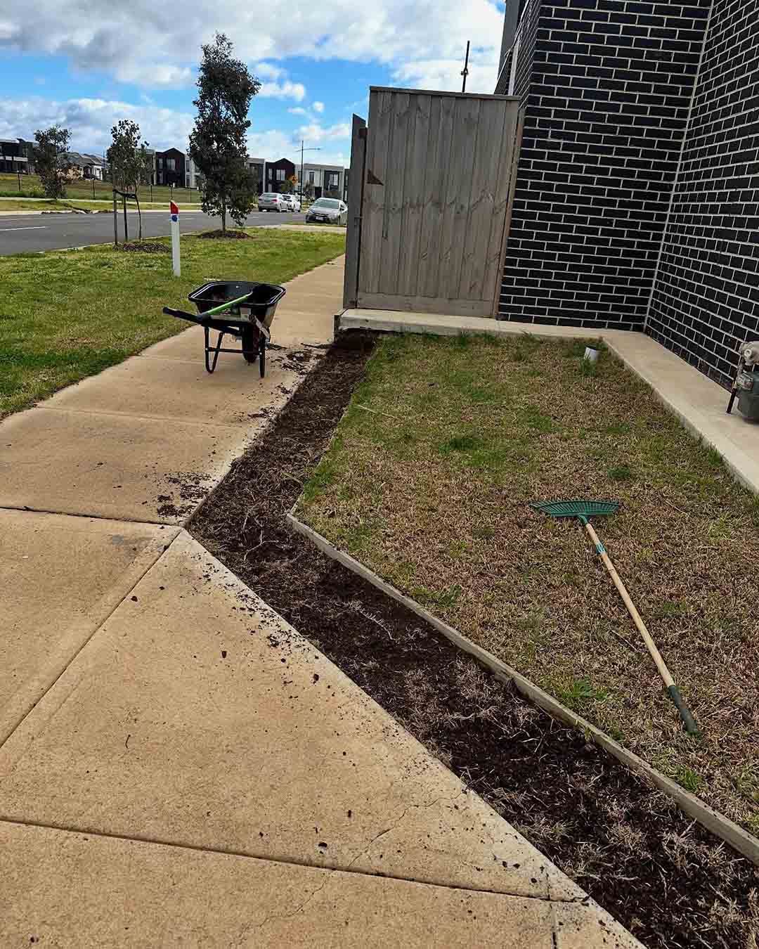 Freshly edged garden bed and lawn beside a footpath, with a wheelbarrow and rake