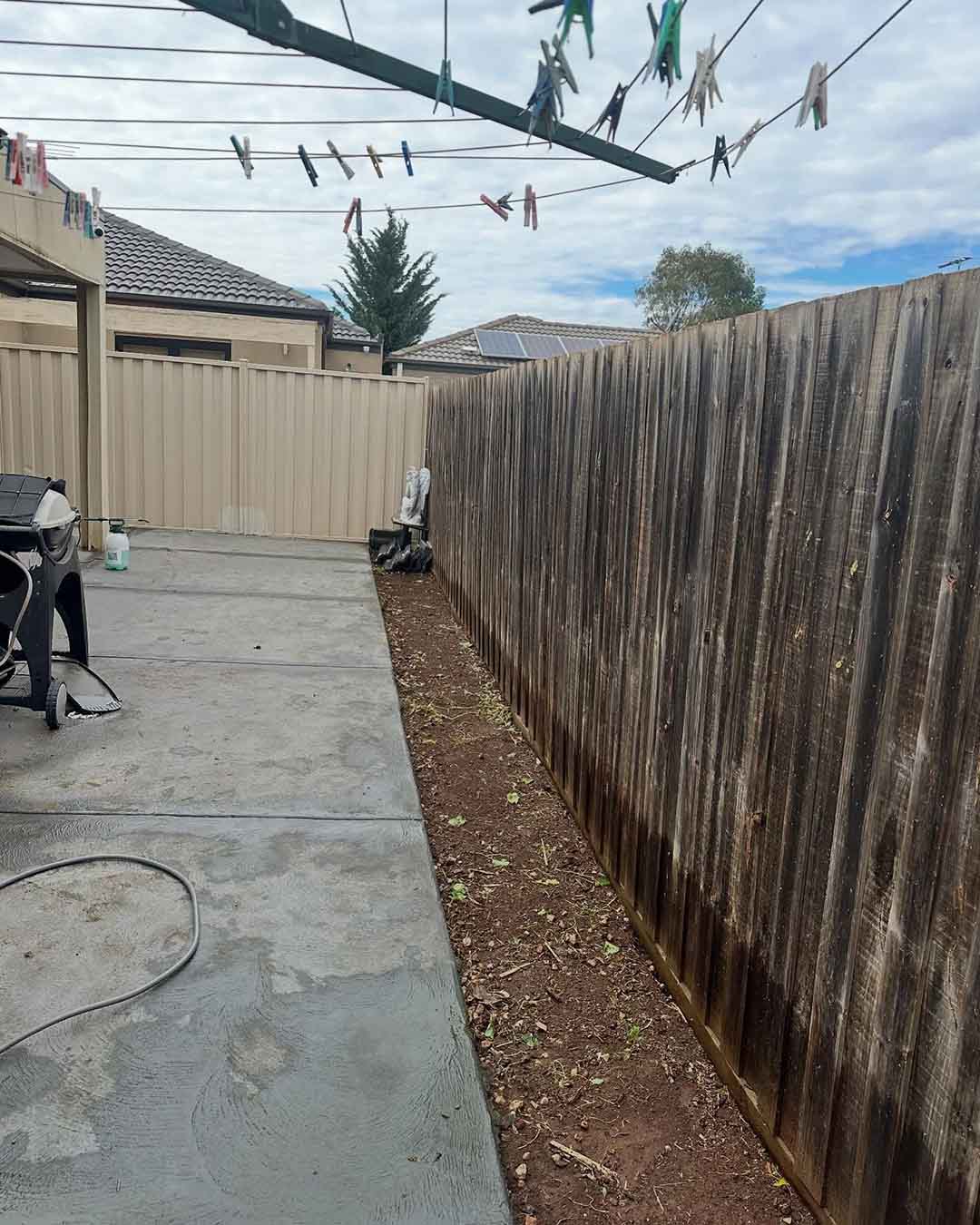 Cleared garden strip along a timber fence beside a concrete courtyard